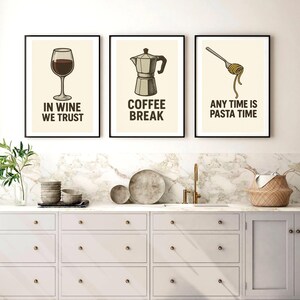 May include: Three framed kitchen art prints. The first features a wine glass with the text "IN WINE WE TRUST". The second shows a coffee maker with the text "COFFEE BREAK". The third shows pasta on a fork with the text "ANY TIME IS PASTA TIME".