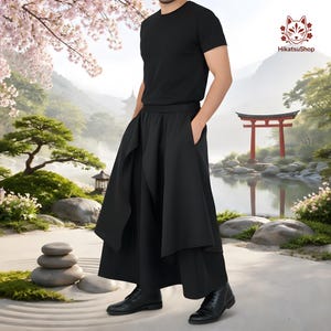 May include: Black hakama trousers with a layered design, worn with a black t-shirt and boots. The trousers have a wide, flowing silhouette. The background shows a Japanese garden scene with a red torii gate and a pond.