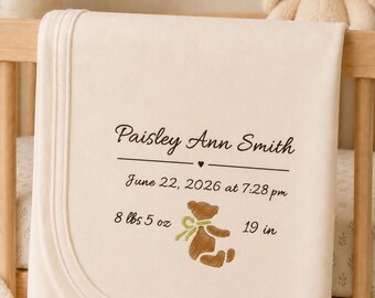 May include: A cream-coloured baby blanket featuring embroidered text that reads Paisley Ann Smith, June 22, 2026 at 7:28 pm, 8 lbs 5 oz, and 19 in. The design includes a small brown teddy bear with a green ribbon and a heart icon.