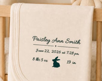 May include: A cream-coloured baby blanket featuring dark green embroidered text that reads Paisley Ann Smith, June 22, 2026 at 7:28 pm, 8 lbs 5 oz, and 19 in, accompanied by a small dark green silhouette of a rabbit centred between the weight and length.