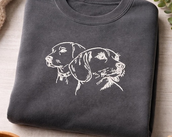 May include: A charcoal grey crewneck sweatshirt featuring a white line art embroidery of two dogs on the front. The design depicts the side profiles of two canine heads with detailed outlines, positioned centrally on the chest of the garment.