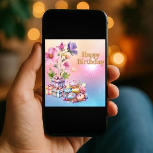 May include: A smartphone displays a watercolor-style birthday card. The card features a floral arrangement with pink and purple flowers, wrapped gifts, cupcakes, and the text "Happy Birthday" in gold.