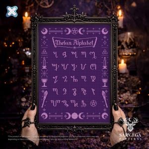 Op de afbeelding: Een ingelijste kruissteek met het Thebaanse alfabet in paars garen op een paarse achtergrond. De zwarte lijst heeft sierlijke details. Het ontwerp bevat manen, sterren, kaarsen en andere symbolen. De tekst "Theban Alphabet" staat bovenaan.