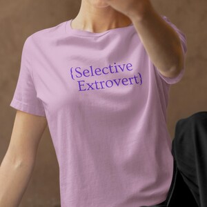 May include: A light purple t-shirt with the text "{Selective Extrovert}" in dark purple. The shirt has short sleeves and a crew neck.