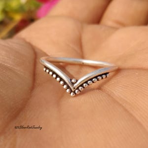 Puede incluir: Un anillo de plata en forma de V con un diseño de cuentas en los bordes. El anillo está enfocado, sobre un fondo borroso. El texto "925SilverRootJewelry" es visible en la parte inferior.