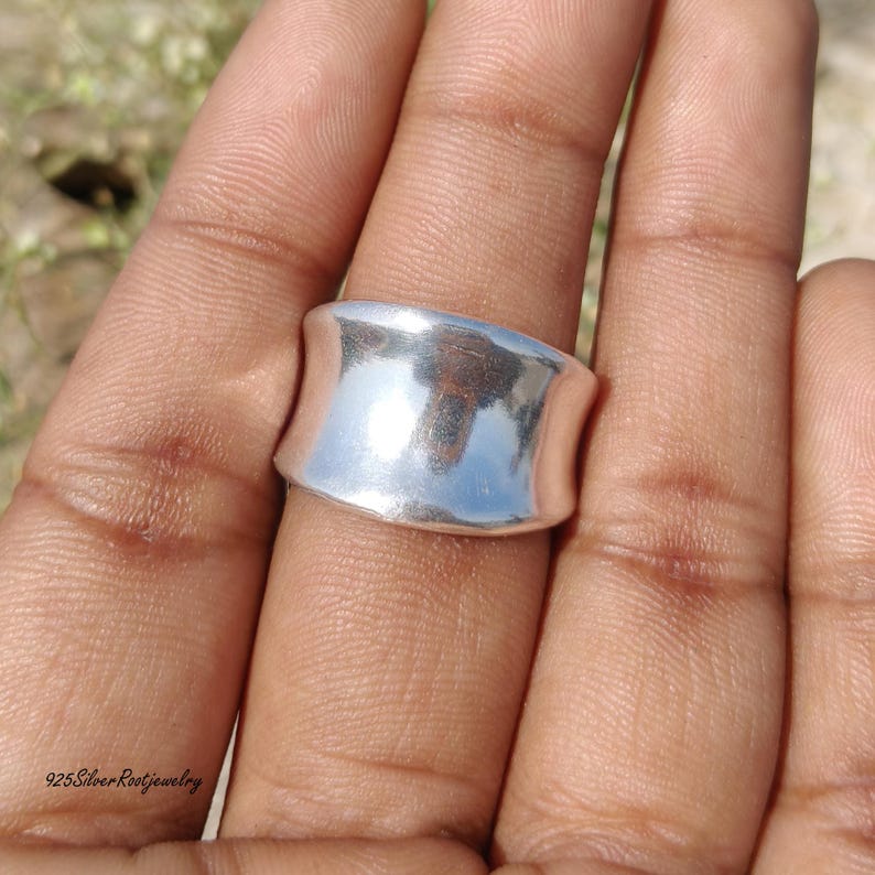 May include: A wide, silver ring with a curved design. The ring is smooth and reflective, catching the light. The text "925 Silver Rootjewelry" is visible at the bottom of the image. This ring is a piece of jewelry.