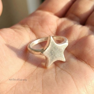 May include: A silver ring featuring a star design. The ring has a brushed metal finish and a simple, modern aesthetic. The text "925 SilverRootJewelry" is visible at the bottom of the image.