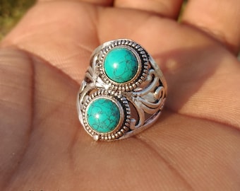 May include: Silver ring with two turquoise stones. The ring has an ornate, filigree design around the stones and along the band. The turquoise stones are a vibrant teal colour, set in a detailed silver setting.