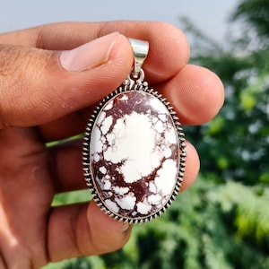 May include: An oval pendant featuring a white stone with dark brown, web-like matrix patterns. The stone is set in a polished silver frame with a decorative beaded edge and a silver bail at the top for attachment to a chain or cord necklace.