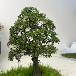 May include: A miniature tree with a textured, dark brown trunk and lush green foliage. The tree sits on a small, round base with vibrant green grass. The model is likely for a diorama or model train set.