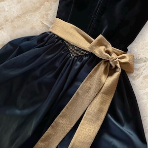 May include: A formal black dress with a gold-colored bow and belt. The dress has a velvet bodice and a flowing skirt. The belt is embellished with small, sparkling details. The bow is tied at the waist.