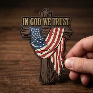 May include: A brown cross-shaped emblem with the text "IN GOD WE TRUST" at the top. The cross features a draped American flag design with red and white stripes and blue stars.