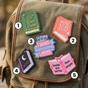 May include: Five book-themed enamel pins attached to a green canvas backpack. The pins feature designs including a green Spell Book, a pink How to be Cute book, a Read More book with flowers, a purple Witch book, and a pink Books are better than people book.