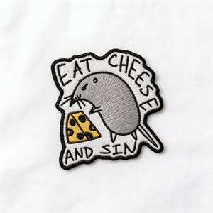 May include: Embroidered patch featuring a gray mouse holding a slice of yellow cheese with black holes. The patch has the text "EAT CHEESE AND SIN" in black lettering, outlined in black. The patch is on a white background.