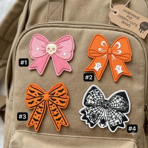 May include: Four PVC bows with Halloween themes. Bow #1 is pink with a skull and stars. Bow #2 is orange with white ghosts. Bow #3 is orange with black bats. Bow #4 is white and black with a spider web and spider pattern. Each bow is numbered.