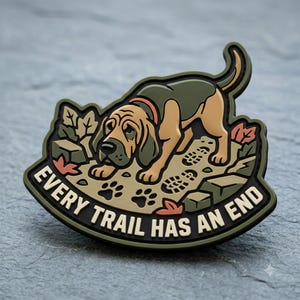 May include: A rubberized patch featuring a tan and olive green bloodhound tracking a scent on a trail with footprints and leaves. The text EVERY TRAIL HAS AN END is printed in bold cream letters along the bottom edge of the dark olive border.