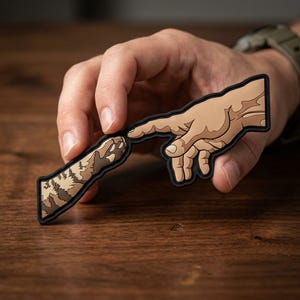 May include: A patch featuring a stylized illustration of two hands touching. One hand is human, the other is a cat paw. The design is in shades of brown and tan with a black border, reminiscent of the Creation of Adam.