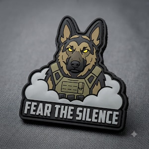 May include: A tactical morale patch featuring a German Shepherd dog wearing a tan plate carrier vest. The dog has glowing yellow eyes and is surrounded by white clouds. The text FEAR THE SILENCE is printed in bold white letters on a black base.