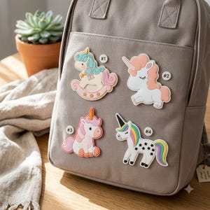 May include: A taupe canvas backpack featuring four distinct unicorn-themed silicone patches labeled #1 through #4. The patches include a rocking horse unicorn, a peach-maned unicorn, a seated pink unicorn, and a white unicorn with black stars.