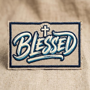 May include: A rectangular patch with the word "BLESSED" in white, outlined in teal, and a teal border. A cross is above the word. The patch is on a tan fabric background.