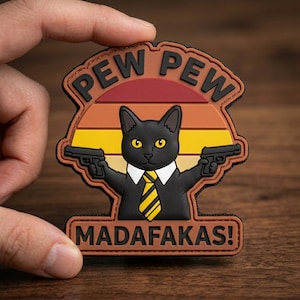 May include: A black cat patch with yellow eyes, wearing a white shirt and yellow tie, holding two guns. The patch has the words "PEW PEW" above the cat and "MADAFAKAS!" below, set against a sunset background.