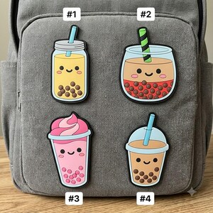 May include: Four silicone patches shaped like bubble tea drinks with smiling faces. Patch #1 is yellow with brown pearls, #2 is brown with red pearls and a green striped straw, #3 is pink with pink pearls, and #4 is tan with brown pearls.