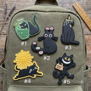 May include: Five black cat rubber patches labeled #1 through #5. #1 is a cat in a green bottle, #2 has pink flowers, #3 is a cat with a candle, #4 is a cat with a yellow sun, and #5 is a grinning cat holding a tan bag labeled TAKE OUT.