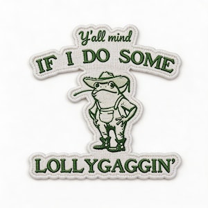 May include: Embroidered patch featuring a cartoon frog in overalls and a cowboy hat. The patch has the text "Y'all mind if I do some lollygaggin'" in green lettering on a white background. The frog is green and white.