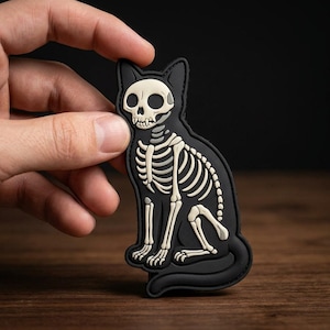 May include: A black cat-shaped patch featuring a white skeleton design. The patch has a detailed depiction of a cat skeleton, including the skull, ribs, and leg bones. The patch is made of a durable material and is suitable for clothing or accessories.