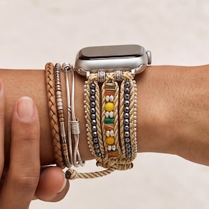 May include: A multi-strand watch band featuring a braided tan cord, metallic silver beads, and a central section with yellow, green, and orange cylindrical beads. The band attaches to a silver smartwatch case and includes additional stacked bracelets.