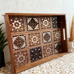 May include: A rectangular wooden serving tray with a decorative tile design. The tiles are in shades of brown, black, and white, featuring floral and geometric patterns. The tray has integrated handles for easy carrying and is ideal for serving food or drinks.