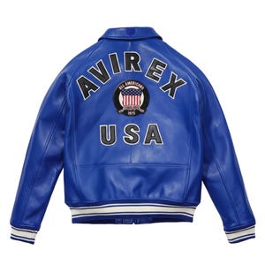 Könnte beinhalten: Eine leuchtend blaue Lederjacke mit dem Text "AVIREX" und "USA" auf dem Rücken. Die Jacke hat einen runden Aufnäher mit einem amerikanischen Flaggen-Design und den Worten "ALL AMERICAN" und "ESTABLISHED 1975". Die Manschetten und der Saum haben weiße und blaue Streifen.