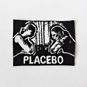 May include: A rectangular black fabric patch featuring a high-contrast white screen-printed graphic of two figures facing each other with their heads bowed. The word PLACEBO is printed in bold white capital letters at the bottom of the patch.