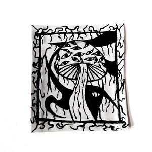 May include: A square patch featuring a black and white ink illustration of a mushroom with multiple eyes covering its cap. The design is enclosed within a rectangular border surrounded by abstract, flowing, vine-like black line patterns.