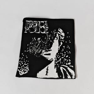 May include: A rectangular black fabric patch featuring a white screen-printed graphic of a person with a distorted face and the text "FRENCH POLICE" in a stylised, jagged font at the top. The design includes scattered white dots and marks.