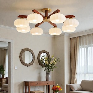 May include: A ceiling light fixture with eight white glass shades. The fixture has a dark brown wooden frame with brass accents. The light is on in a well-lit room with neutral-colored walls and a sofa.