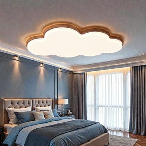 May include: A cloud-shaped ceiling light fixture with a warm wood-tone trim and a bright white center. The light is installed in a bedroom with a bed, curtains, and a window. The room has a blue-gray color scheme.