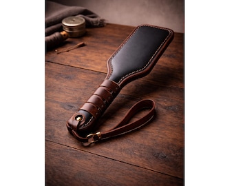Pala de cuero auténtico hecha a mano en contraste negro y marrón, correa para la muñeca y mango ergonómico.
