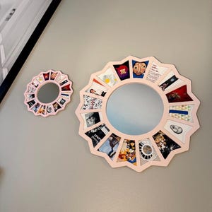 May include: Two circular wall mirrors with light pink frames featuring a scalloped, star-like edge. Each mirror is surrounded by a series of small, square, multi-coloured graphic art prints arranged in a radial pattern around the central glass.