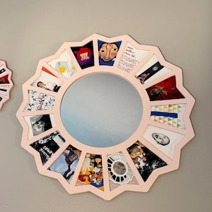 May include: A circular wall mirror with a light pink, star-shaped frame. The frame features sixteen individual compartments, each containing a different small square image or graphic print, surrounding a central circular reflective glass surface.