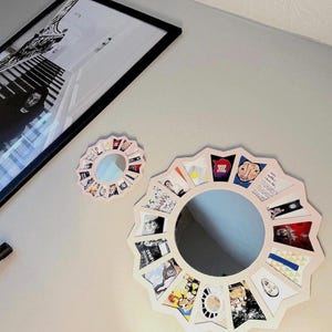 May include: Two circular mirrors with scalloped, light-coloured frames. The larger mirror features a border of small, colourful rectangular images arranged in a radial pattern. A smaller, matching mirror sits above it, also surrounded by tiny images.