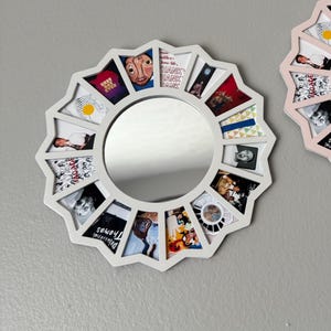 May include: A circular white frame with a starburst edge featuring a central round mirror surrounded by twelve trapezoidal photo slots. Each slot contains a different small image, including text that reads "BEST DAY EVER", "THANK YOU", and "Delusional Thomas".