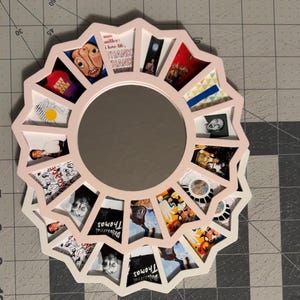 May include: A circular wall mirror with a light pink frame featuring a starburst edge. The frame contains multiple small, triangular photo inserts displaying various album art and imagery, including text reading Mac Miller and Delusional Thomas.