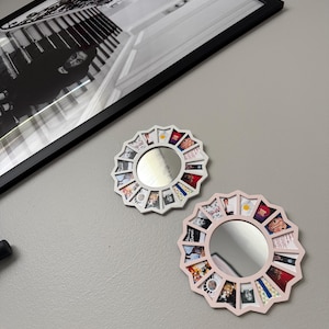 May include: Two circular wall mirrors with white and light pink frames, each featuring a series of small, colourful square photo inserts arranged in a sunburst pattern around the central reflective glass surface.