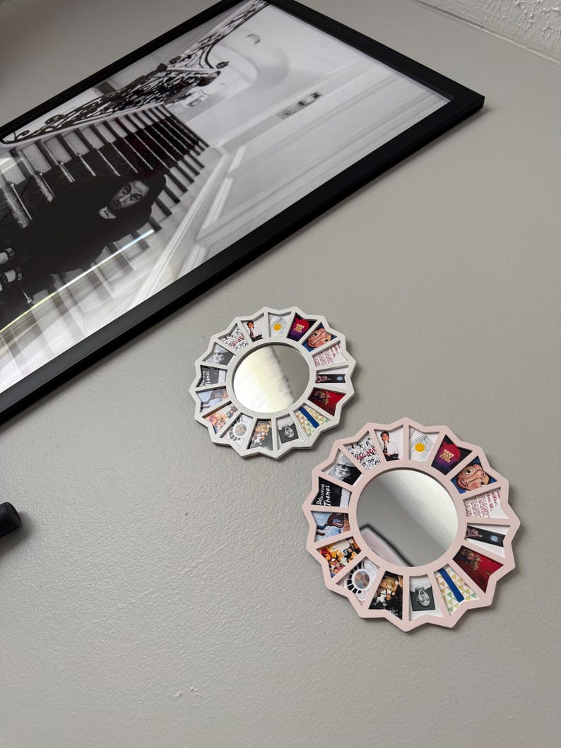 May include: Two circular wall mirrors with white and light pink frames, each featuring a series of small, colourful square photo inserts arranged in a sunburst pattern around the central reflective glass surface.