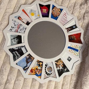 May include: A white circular collage frame featuring a central round mirror surrounded by twelve trapezoidal photo slots. The frame displays various album art prints, including text that reads "BEST DAY EVER", "mac miller: i love life, THANK THANK THANK", and "Delusional Thomas".
