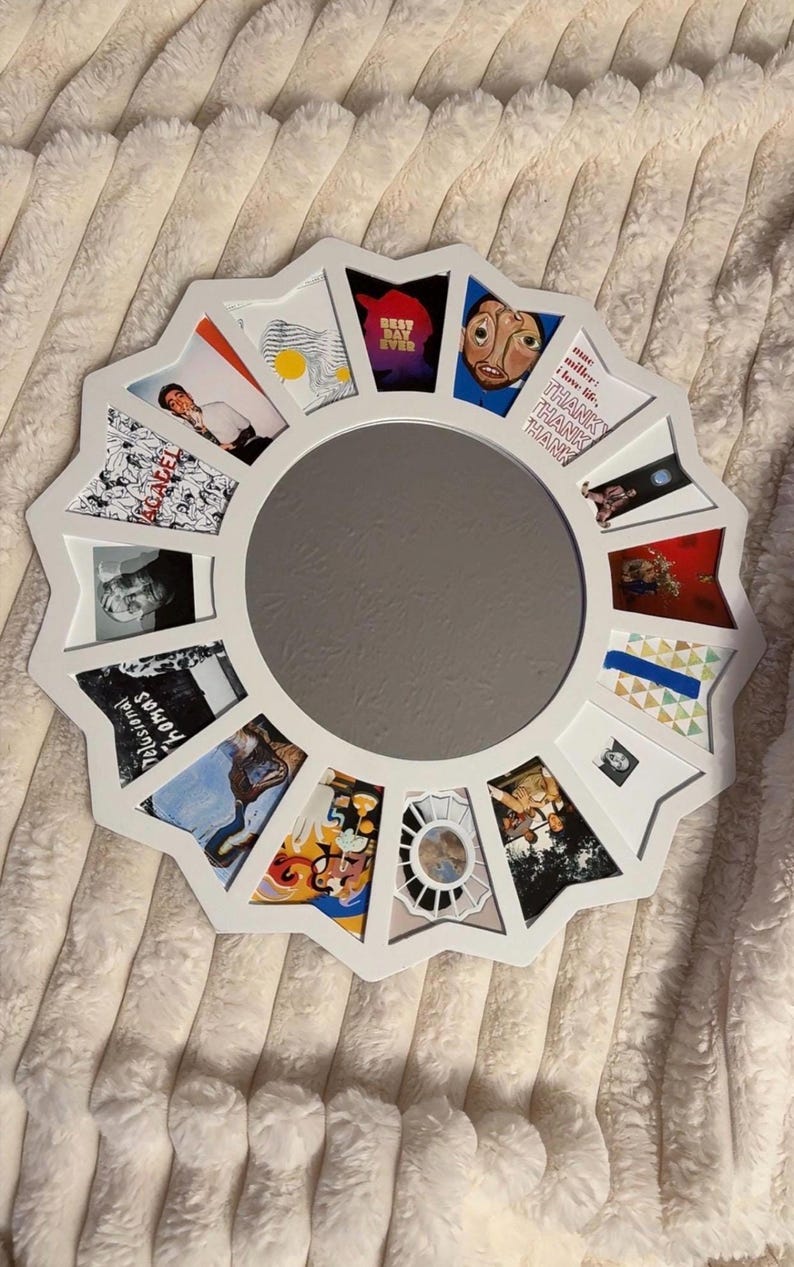 May include: A white circular collage frame featuring a central round mirror surrounded by twelve trapezoidal photo slots. The frame displays various album art prints, including text that reads "BEST DAY EVER", "mac miller: i love life, THANK THANK THANK", and "Delusional Thomas".
