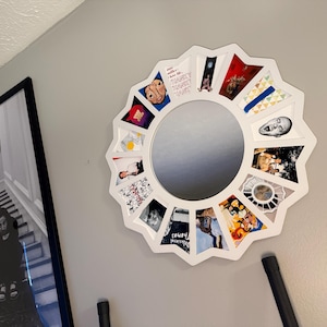 May include: A white, star-shaped wall mirror featuring a circular centre and twelve surrounding triangular compartments. Each compartment contains a distinct, colourful graphic illustration or photograph, creating a collage effect around the mirror.