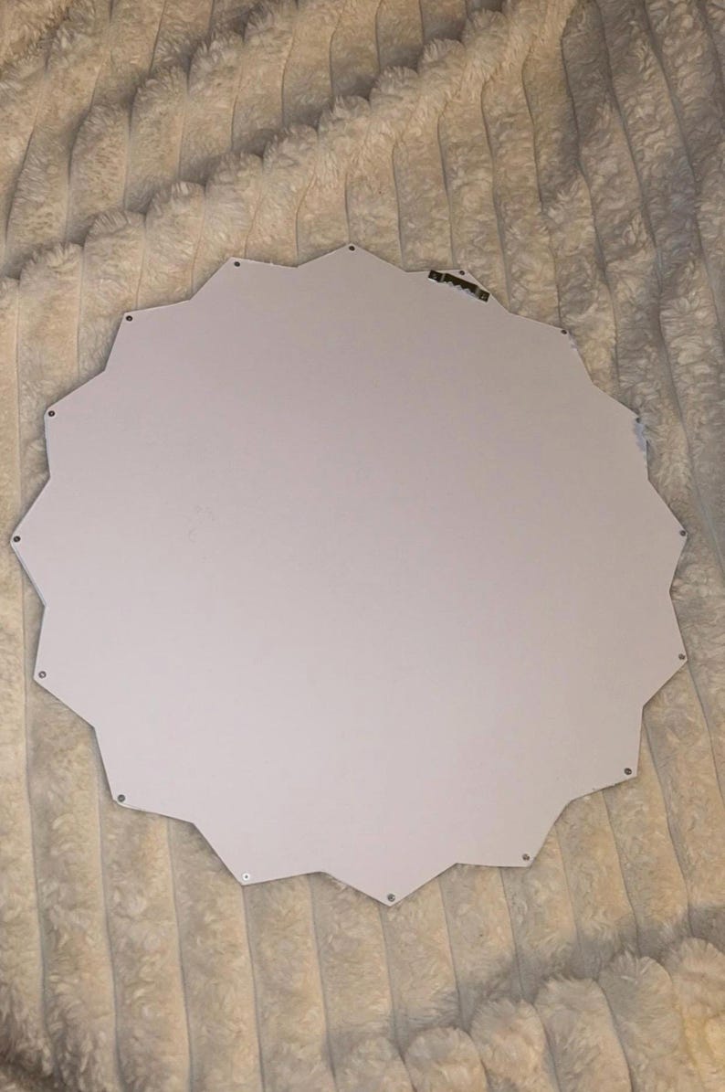 May include: A white, star-shaped wall mirror backing with a smooth, flat surface. The edges feature a jagged, multi-pointed silhouette. A small, metallic sawtooth hanger is attached to the upper portion of the back for mounting purposes.