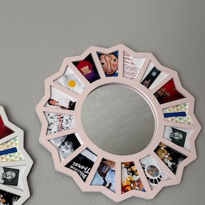 May include: A circular wall mirror with a light pink, star-shaped frame featuring twelve trapezoidal compartments surrounding the central glass. Each compartment displays a unique small image, including text such as "Best Day Ever" and "Delusional Thomas."